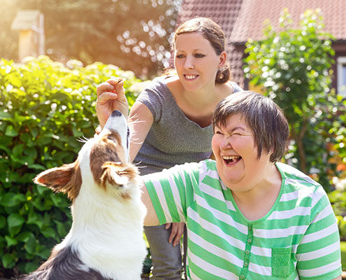 A mentally disabled woman happily trains a dog with the guidance of a female caretaker.