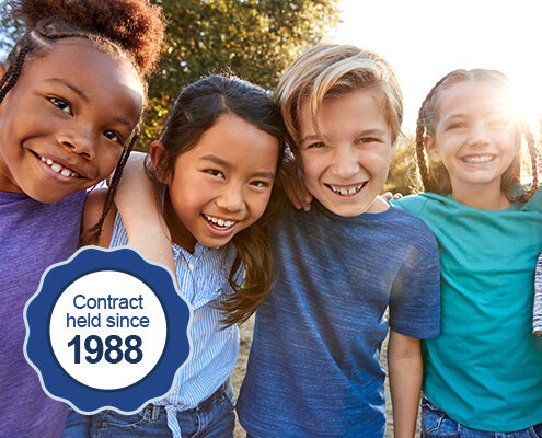 Diverse children link arms and pose for a portrait with trees and sunshine in the background. On the image is a badge that reads, "contract held since 1988".
