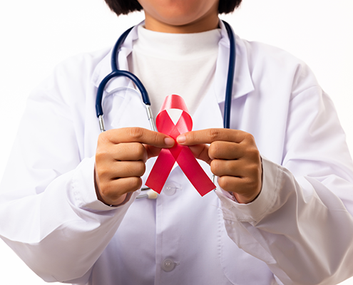 A doctor in white scrubs holds a red ribbon.