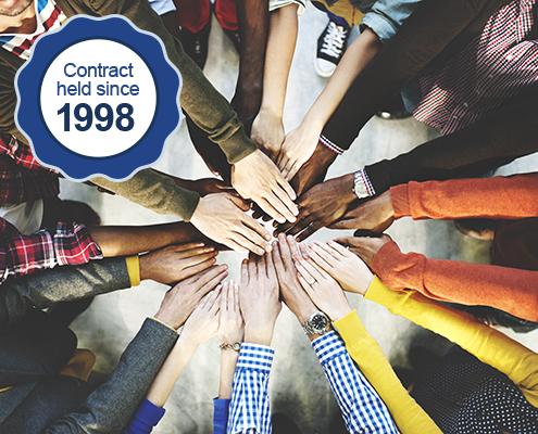 Diverse hands reach together in a circle indicating a large team working together. A graphic badge on the image reads, "Contract held since 1998".
