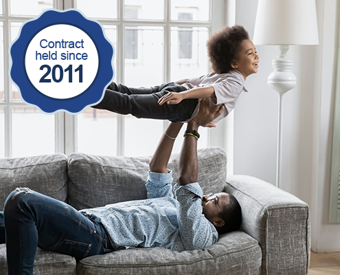 A father plays airplane with his son on a couch. A icon indicates WRMA has held this contract since 2011.