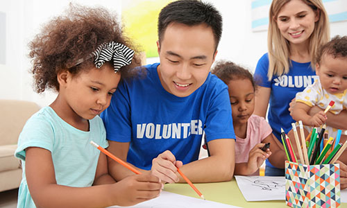 Young male volunteer drawing with young children at table.