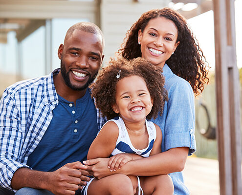 A happy Black family portrait, with a mother, father, and their young daughter.