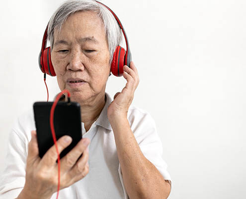 Senior Asian woman listens closely to her mobile device using headphones.
