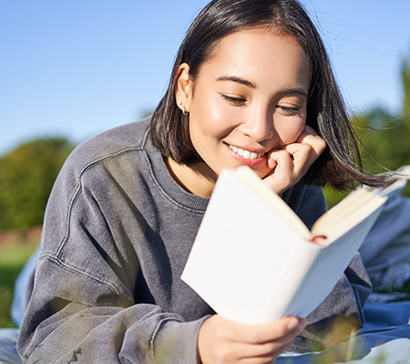 Young woman lying down outdoors enjoying a book.