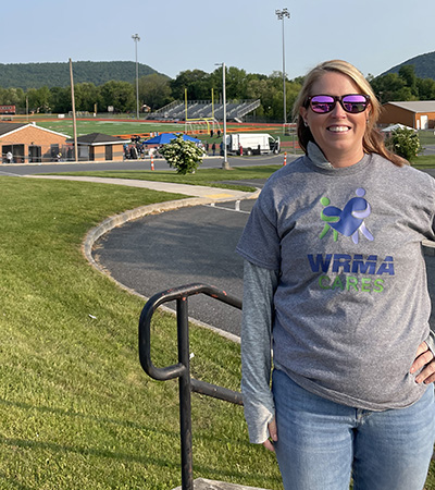 Carissa Woleslagle stands smiling outside with athletic fields in the background.