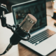 Close-up of a microphone with a laptop on the table. The laptop shows a video conference.