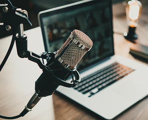 Close-up of a microphone with a laptop on the table. The laptop shows a video conference.